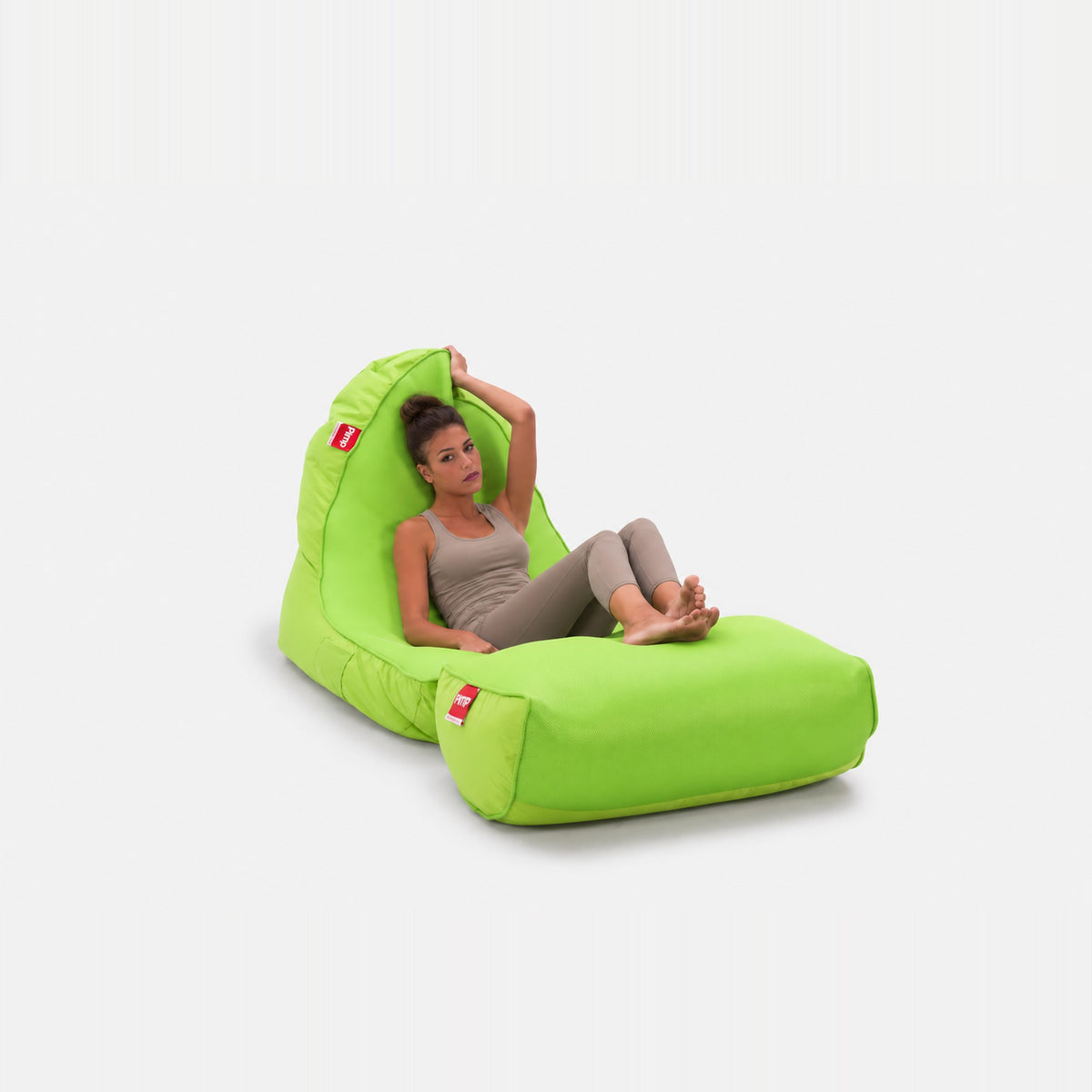 Woman relaxing on the PIMP Coolio Wild Lime beanbag sofa and matching ottoman, front three-quarter view